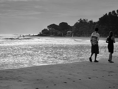 gray scale photography of man and woman walking on seashore thumbnail