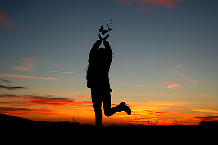 silhouette of person standing under orange clouds during sunset thumbnail