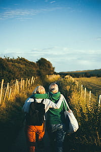 two woman walking on the road in between fields during daytime photography thumbnail