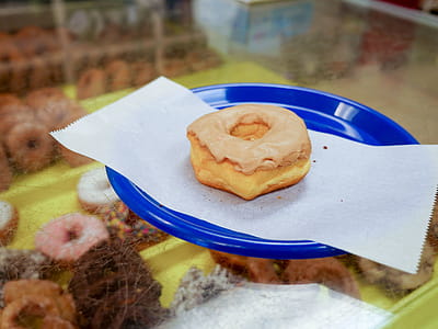 maple donut sitting on a blue plate in a donut shop. thumbnail