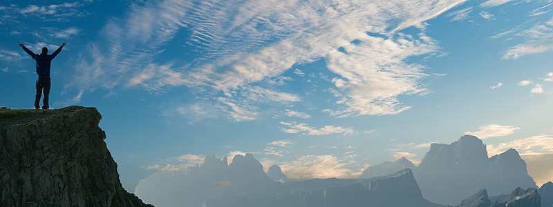 silhouette person standing on cliff while raising both hands thumbnail