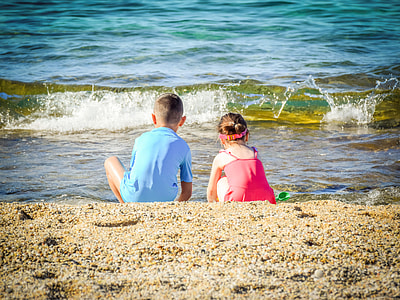 two boy and girl sitting on sand at the beach thumbnail