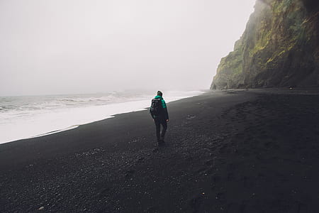 man wearing backpack while walking on seashore thumbnail