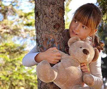girl embracing tree while holding bear plush toy thumbnail