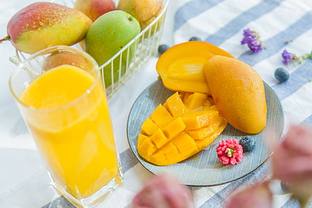three mangoes and filled pint glass on white and blue striped table thumbnail