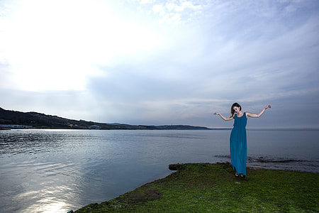 woman in blue long dress standing beside the body of water thumbnail