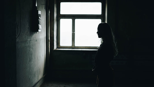 silhouette of woman standing facing in wall inside the dark room thumbnail