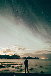man standing near body of water under stars thumbnail