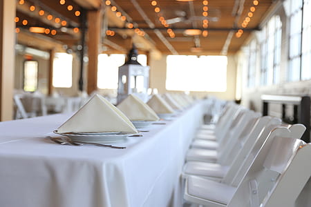 white folded napkins on white covered table beside white metal armchairs thumbnail