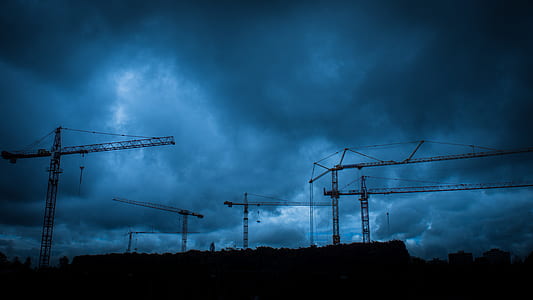silhouette of construction cranes under cloudy sky during daytime thumbnail
