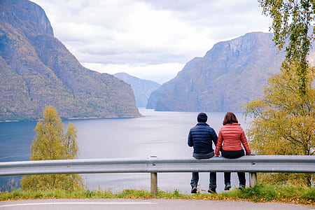couples sitting on road guardrail facing body of water and mountain thumbnail