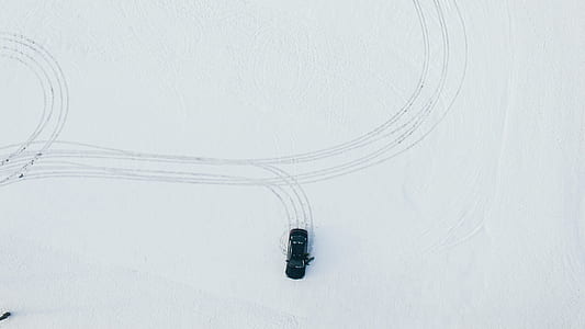 black car driving through snow-covered pavement thumbnail