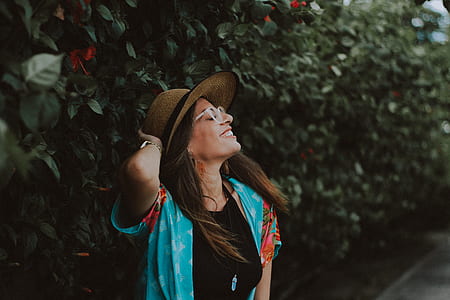 woman wearing hat looking up near green leafed wall plant thumbnail