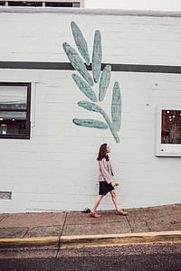 woman walking on pathwalk beside white concrete building thumbnail