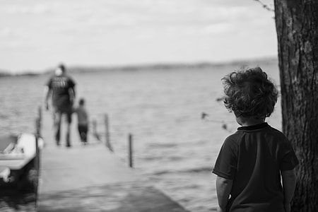grayscale photo of boy beside tree looking at father and son walking on dock thumbnail