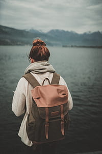 woman in white jacket with brown backpack standing over body of water thumbnail