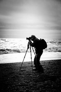 grayscale photography of man taking picture at the sea thumbnail