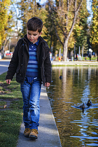 boy in blue and white stripe polo shirt and blue denim jeans walking near body of water thumbnail