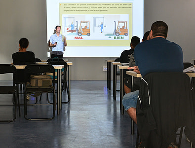 man beside projector projection showing forklifts in front of group of people sitting on chairs thumbnail
