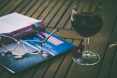 wine glass filled with liquor beside book and eyeglasses thumbnail