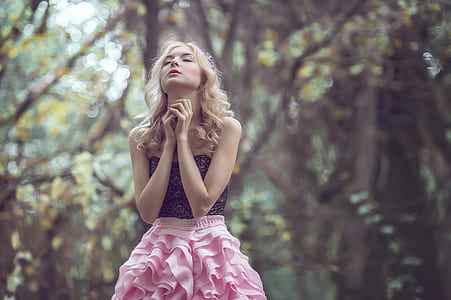 woman closing eye while taking photo under tall trees at daytime thumbnail