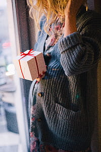 Woman Wearing Blue Knit Cardigan Holding Gift Box Inside Room thumbnail