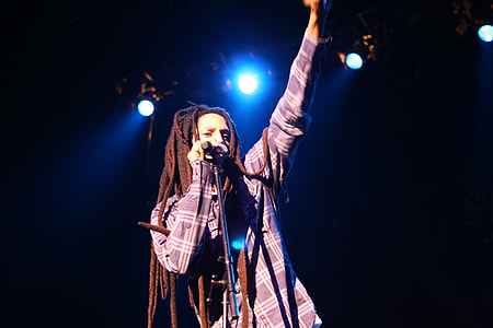 dread-lock haired man standing holding microphone on stage thumbnail