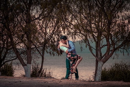 man and woman kissing in middle of two brown trees thumbnail