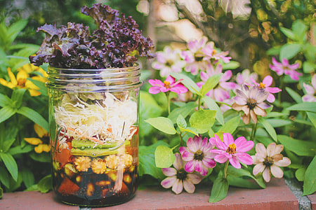 clear glass jar surrounded by purple, yellow and white petaled flowers thumbnail