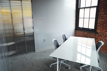 rectangular white wooden table with three vacant rolling chairs thumbnail