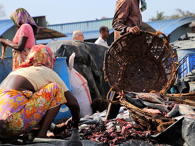 man holding basket in in front of woman cleaning fish organs on ground thumbnail