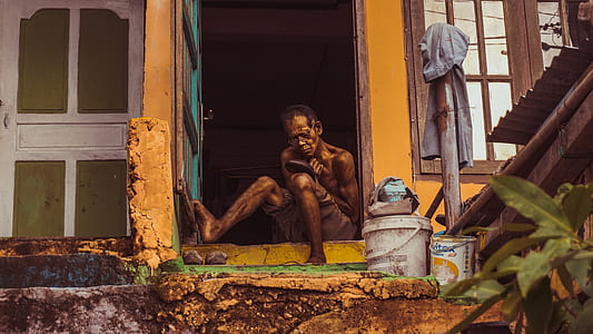 man sitting beside green metal door during daytime thumbnail