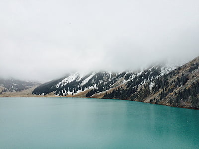 body of water near mountain with snow during daytime thumbnail