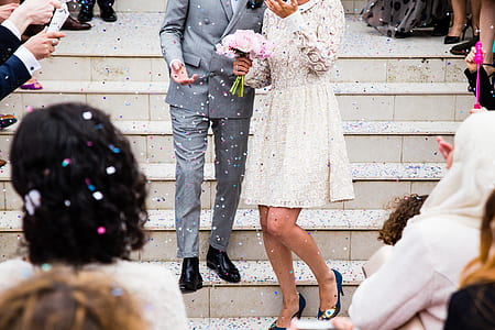 woman in white lace long-sleeved dress and man win grey suit walking downstairs with people on side thumbnail