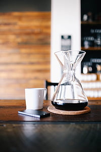 selective focus photography of clear pitcher beside white ceramic mug and phone on brown wooden table thumbnail