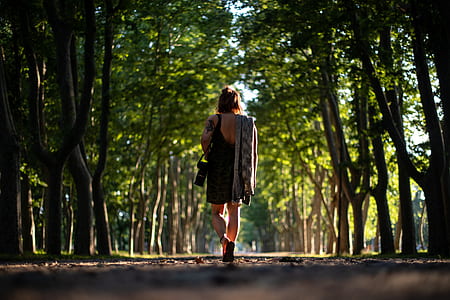 woman walking pathway between green leafed trees thumbnail