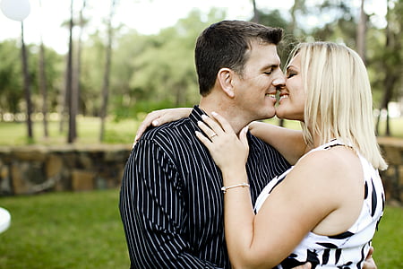 man wearing black and white striped collared long-sleeved shirt hugging a woman wearing white and black floral sleeveless top thumbnail