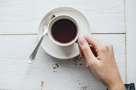 person holding cup of coffee on white saucer beside spoon thumbnail