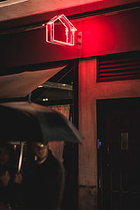 man and woman holding black umbrella near red neon light signage thumbnail
