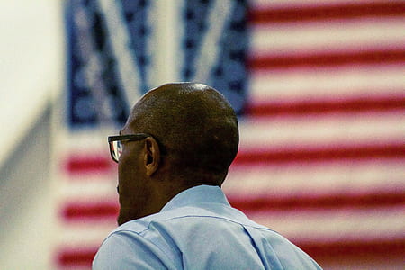 man wearing black framed eyeglasses standing near flag thumbnail