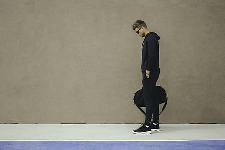 man standing near wall holding duffle bag thumbnail