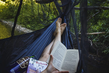 person laying on hammock while reading book during daytime thumbnail
