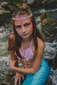 girl wearing mermaid costume sitting on rock thumbnail