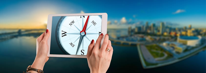 person holding powered-on iPad with compass display thumbnail