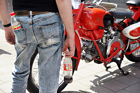man holding Coca-Cola clear plastic bottle standing in front of red and black motorcycle during daytime thumbnail