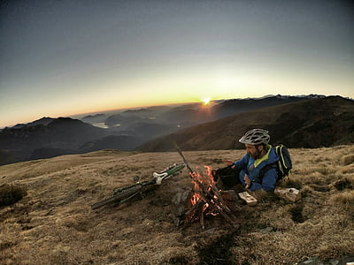 man on mountain with bicycle and setting up bonfire thumbnail