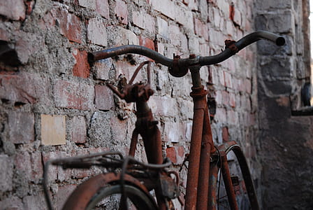 brown bicycle parked beside brick wall thumbnail