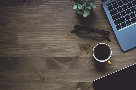 white ceramic mug near eyeglasses with black frames and gray laptop computer on brown table thumbnail