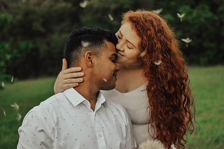 woman kissing man's forehead sitting on green grass near trees thumbnail