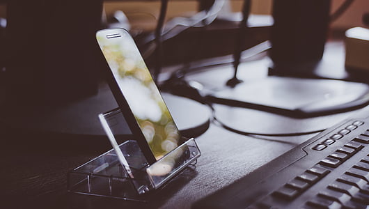 black smartphone on clear glass stand near black computer keyboard thumbnail